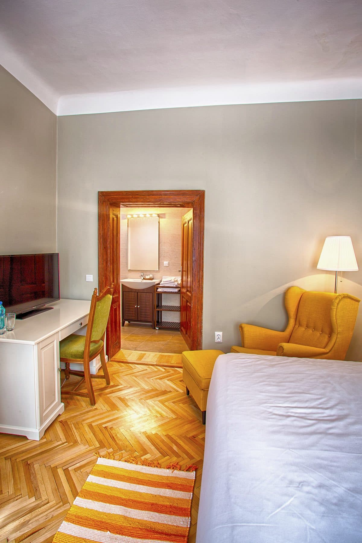 The desk in the standard double room, with its chair, the yellow armchair and the corner of the bed.