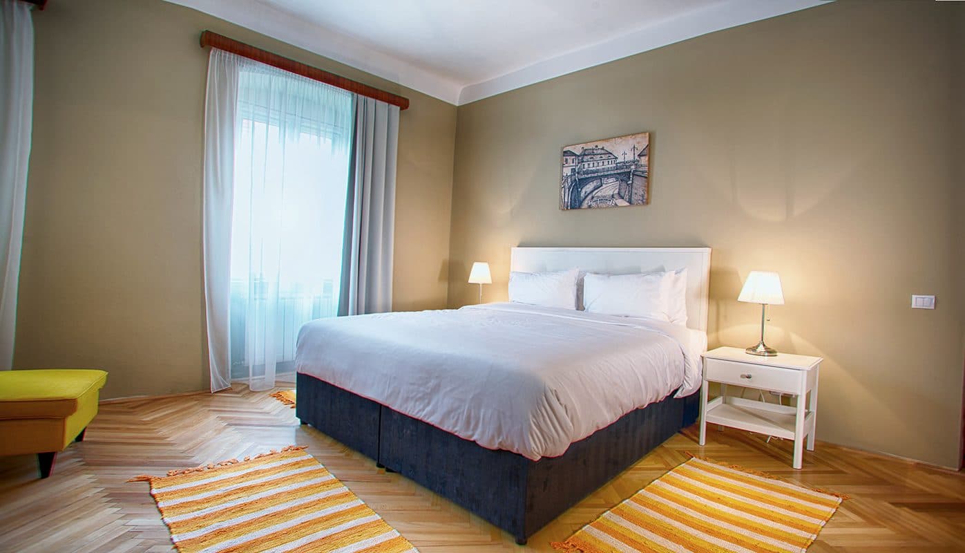 A superior room, with a double bed, a yellow armchair and footstool, and a striped runner.