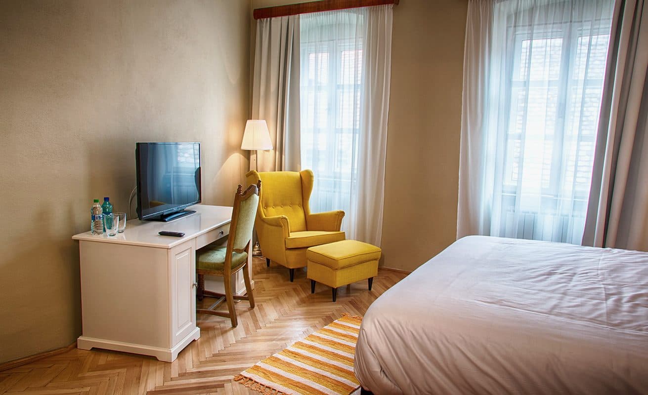 A superior room, with a desk, television, yellow armchair and a double window.
