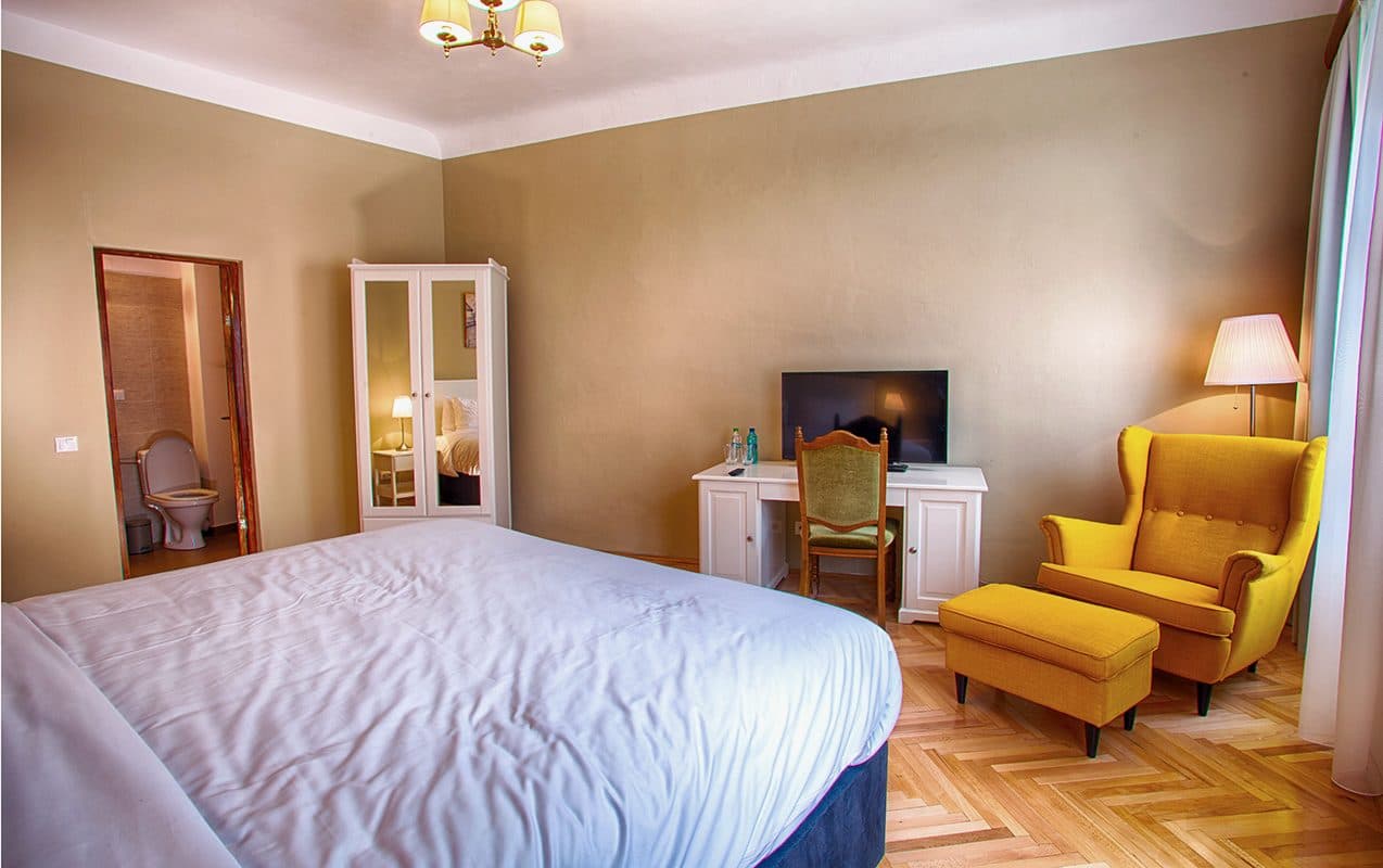 A superior room looking towards the bed, with the yellow armchair, footstool and floor lamp.
