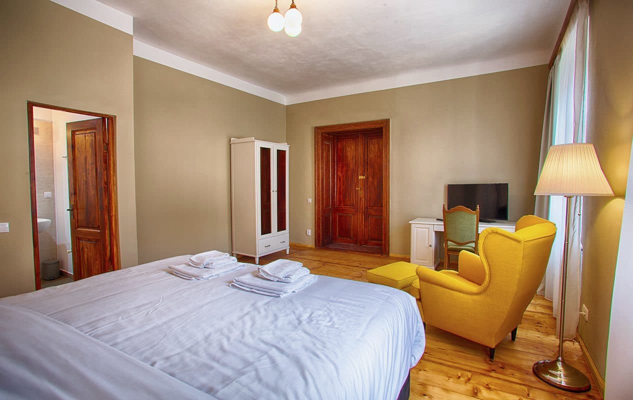 A superior room, with the bed, a tall mirror, a yellow armchair and a chair.
