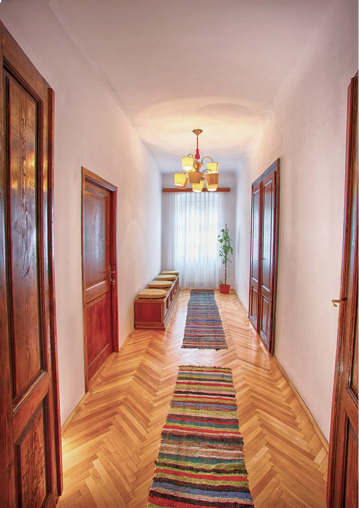 The corridor of the house, with herringbone parquet, tall red-brown double doors and multicoloured woven runners along its length.