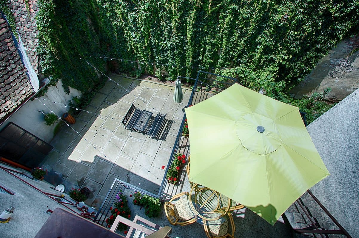 The inner courtyard seen from above: the flagstones, the open parasol, the terrace furniture and the wall of wild vine.