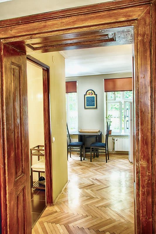 The studio's entrance, through a tall wooden door frame, into the room with its window and table.